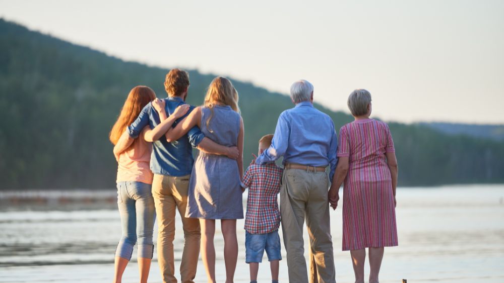 family with grandma and grandpa looking back at the body of water and mountain - 18 Ways to Travel Without Breaking the Bank