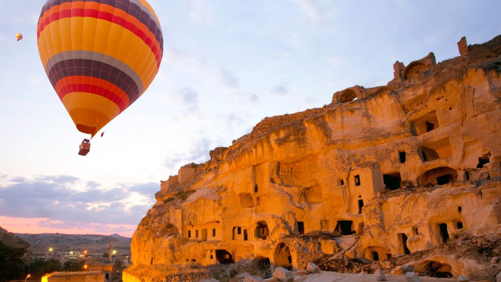 hot air balloon near cave-style accommodations carved into ancient volcanic rock