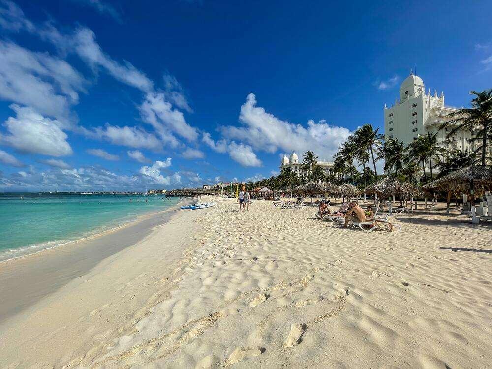 white sand ,blue sky and green beach in Aruba beach with people walking and sitting around the white sand