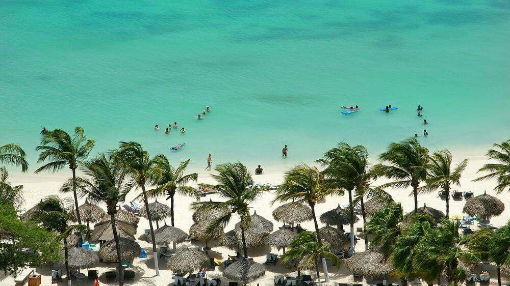 aerial view of the stunning Aruba White Sand Beach with people soaking in the beach also shows nipa huts and coconut trees