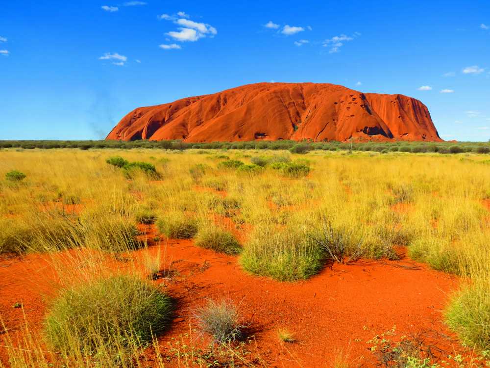 orange/brown mountain in a dessert like hill surrounded by green grass- australia digital nomad visa