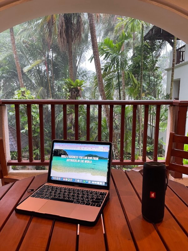 image of a laptop on top of a wooden table with JBL speaker showing coconut trees on the background