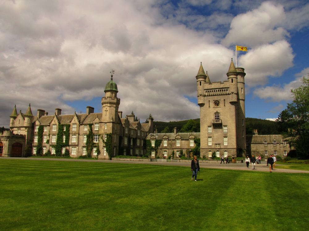 people walking around the green grass near a concrete castle