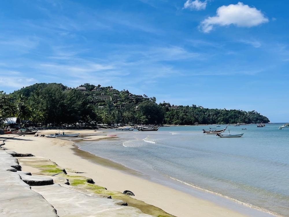 side view of the beach with boat in it and green trees on the side also known as the bang tao beach