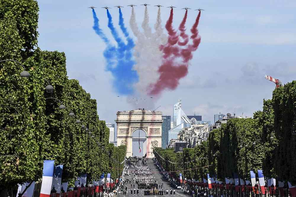 service members march in the street for Bastille Day parade. and smoke trails billow overhead from a flyover