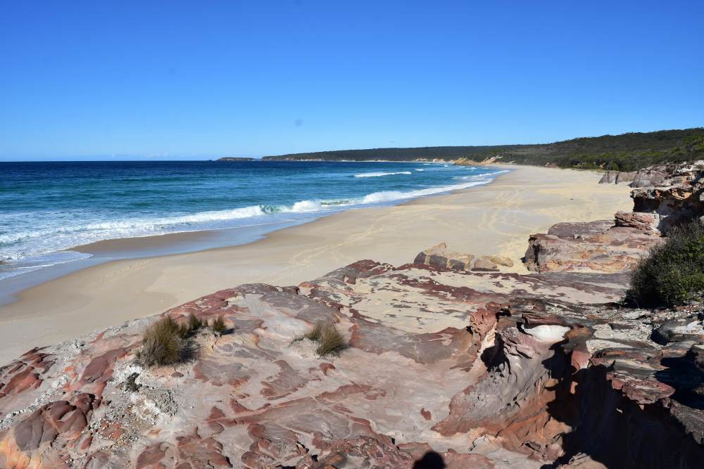 blue sky and blue ocean with golden sand with rocks on it