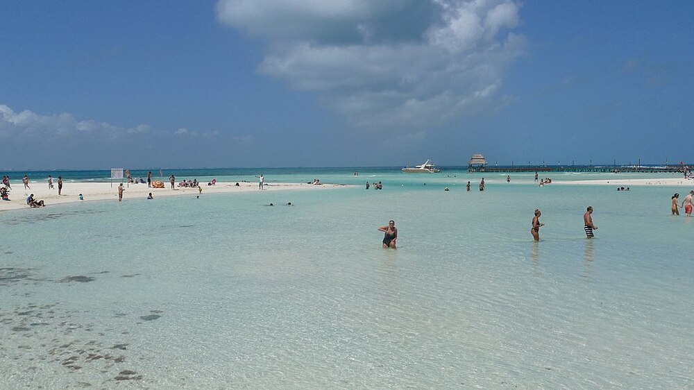people swimming at the shore of a white sand and clear beach 