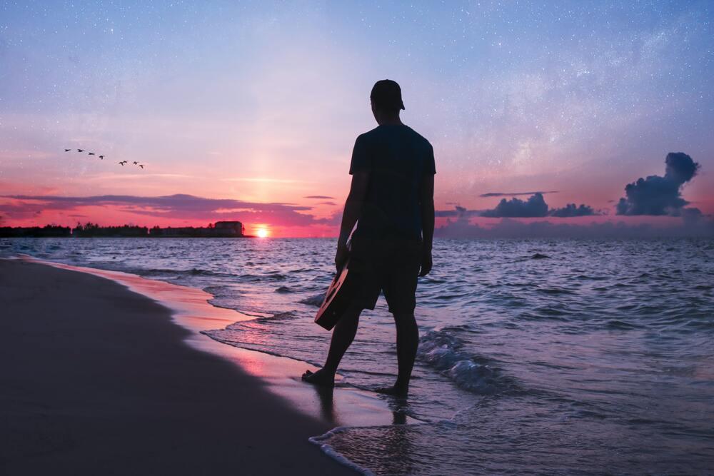 A man on his back holding guitar standing at the seashore at dawn in cable beach