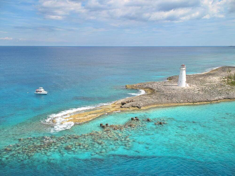 White lighthouse in an island in the middle of the ocean and white boat sailing in the ocean