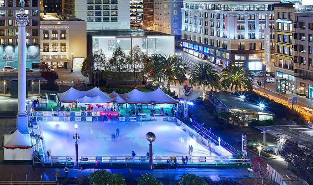 a top view of the lighted union square ice rink during night time with skiers and onlookers