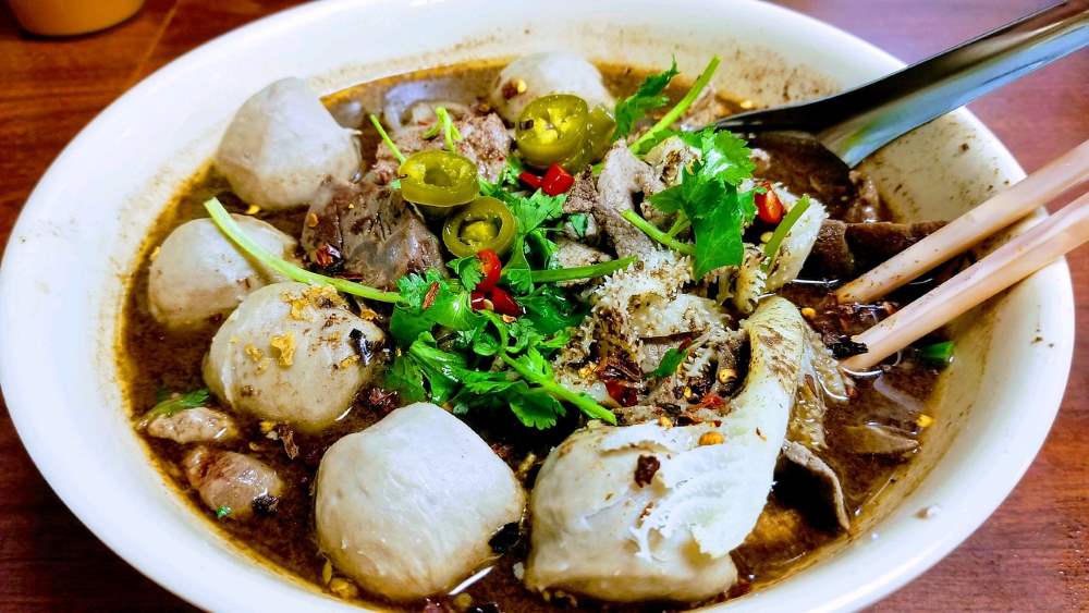 beef or pork in rice noodles in black soup with chopstick on the side - best thai food in thailand