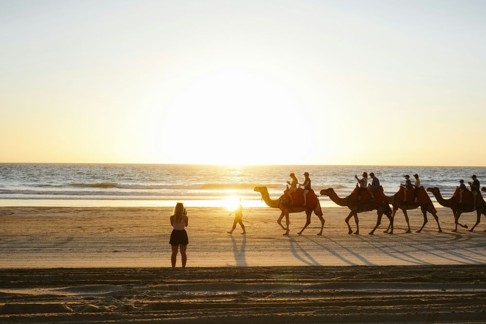 woman in front of the beach with group of people riding camel - Best Places to Visit in Australia