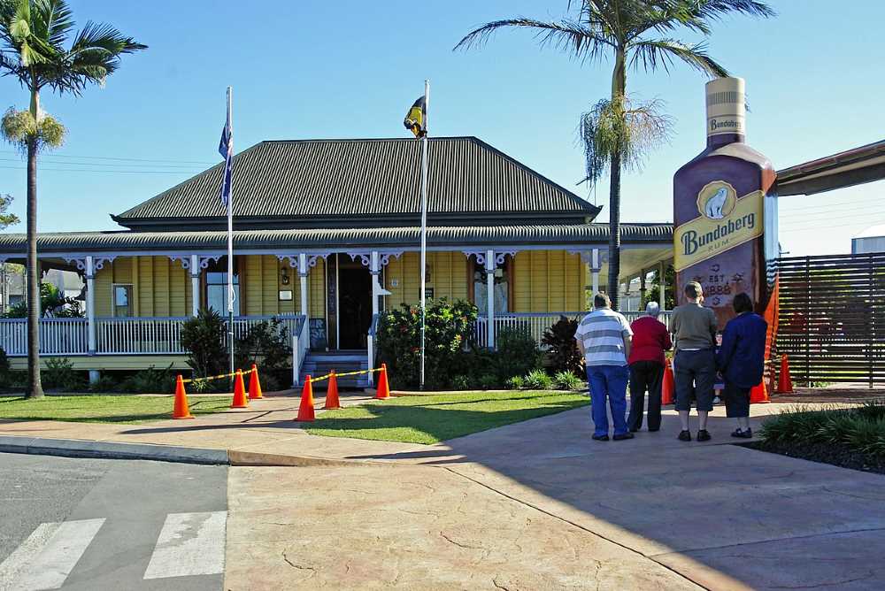 people in front of a human size rum statue near yellow house - Best Places To Visit In Queensland