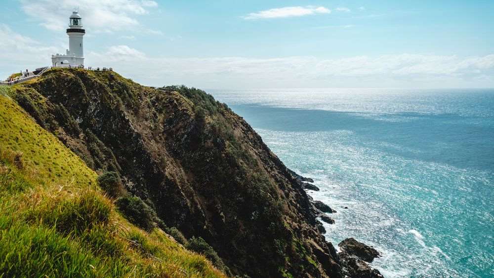 white Cape Byron Lighthouse on top of the hill near the edge beside the ocean