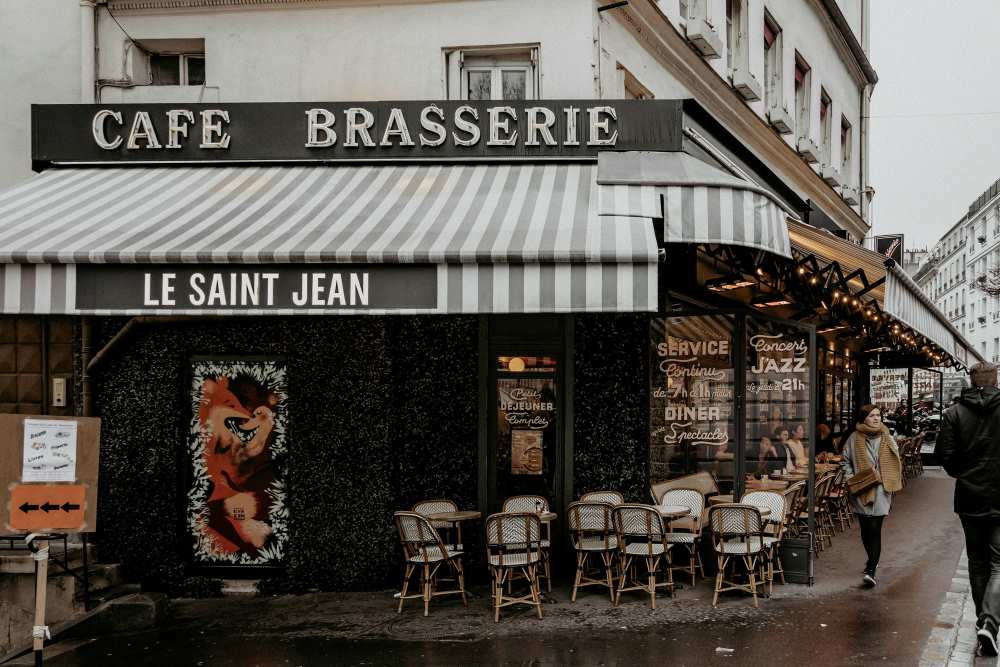 girl passing by the side of the street in front of a cafe with people sitting in outside