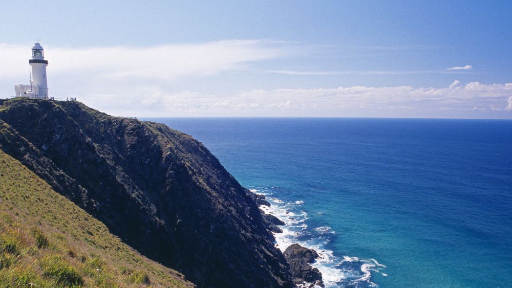 white lighthouse on top of the hill near body of water - Best Beaches Near Brisbane