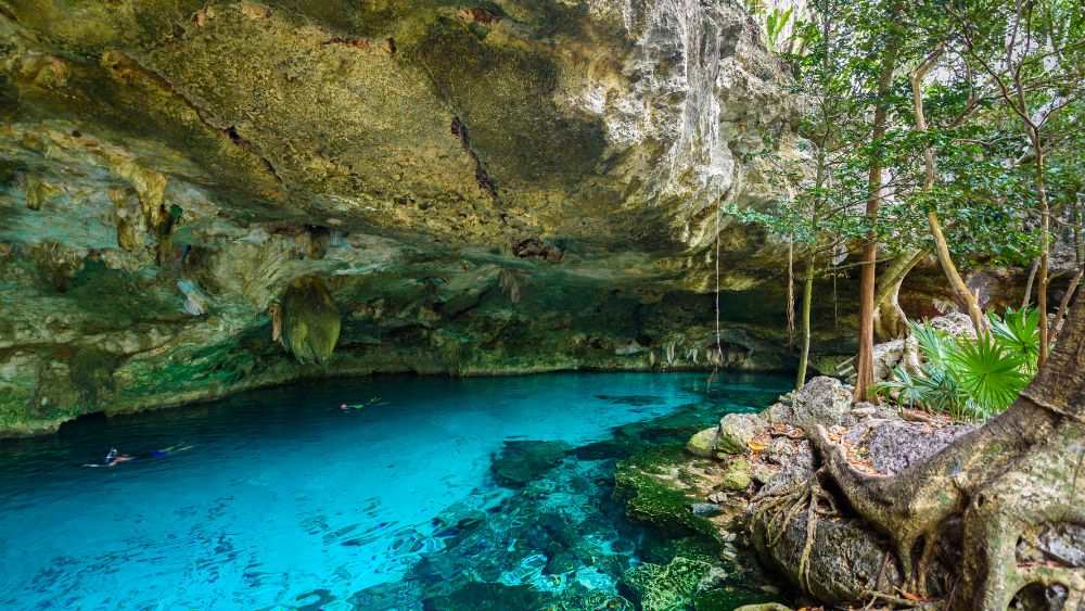 blue body of water in the middle of a rock cave and forest