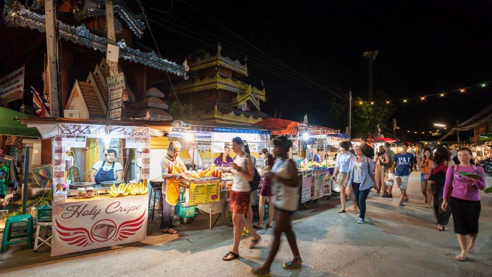 people walking in the street market with stall of foods in the side- things to do in chiang mai