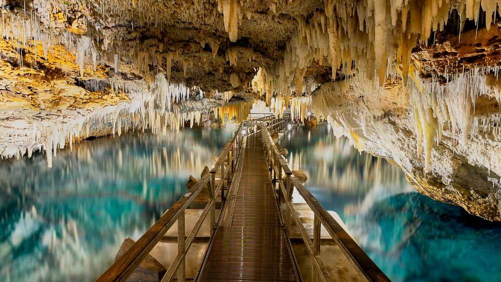  beautiful limestone formations in the ceiling with pathway over clear body of water