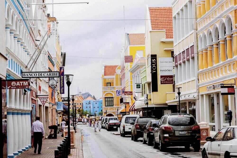 yellow and white buildings with car parked on the side of the street and people walking in Curacao town in Aruba