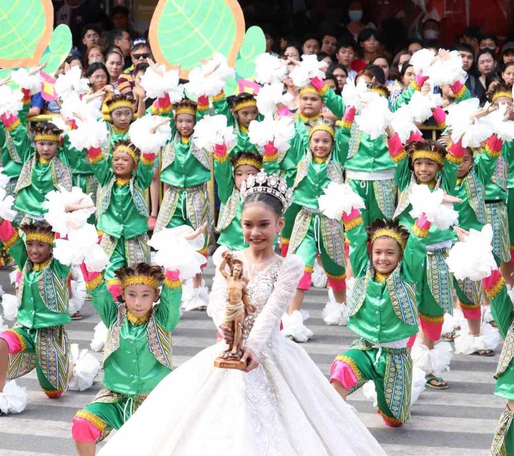 group of children dancing in the street wearing green custom and a little girl in the middle holding statue - philippines vs thailand