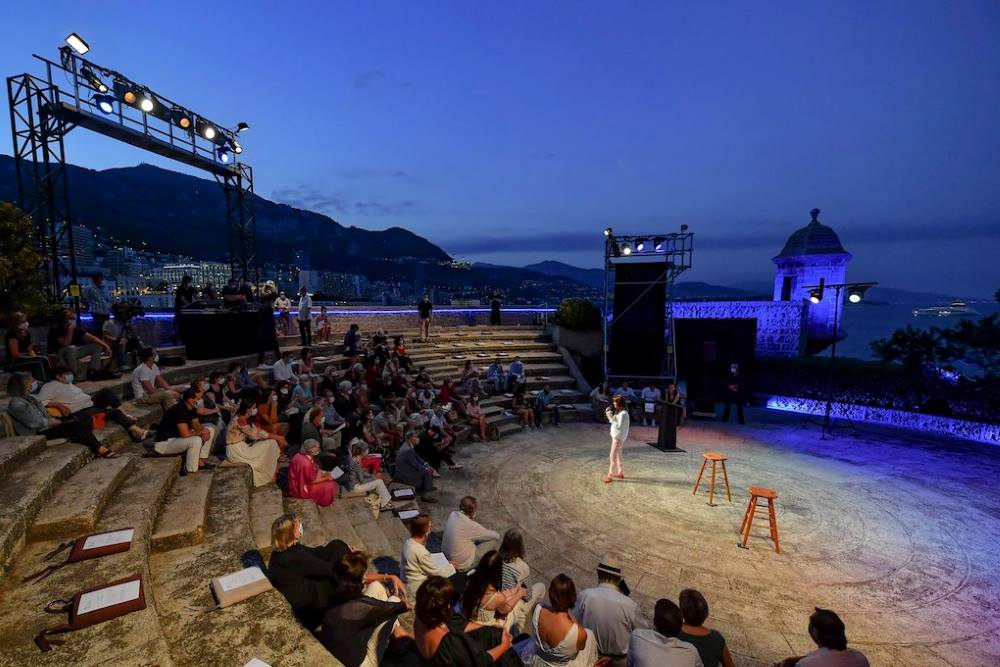 an open-air theater with audience sitting and taking notes