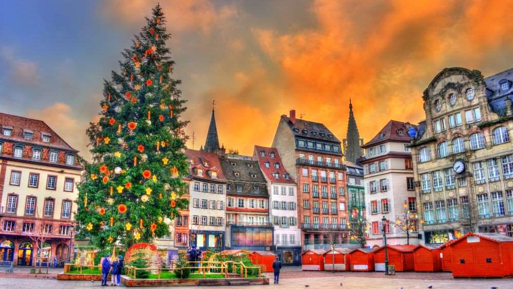 tall christmas tree on the middle of the street surrounded by structure buildings and red house like stores- Best Time to Visit France