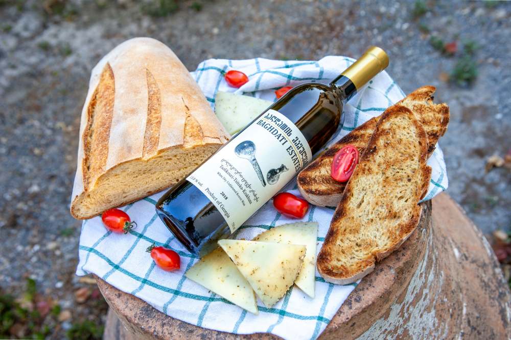 A bottle of Georgian natural wine with fresh bread, cheese, and cherry tomatoes. - best cities for nomads