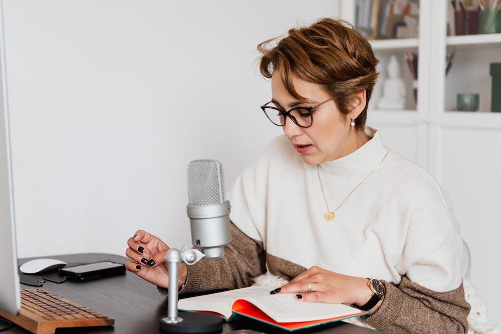 Image of a woman in front of a microphone and reading a book