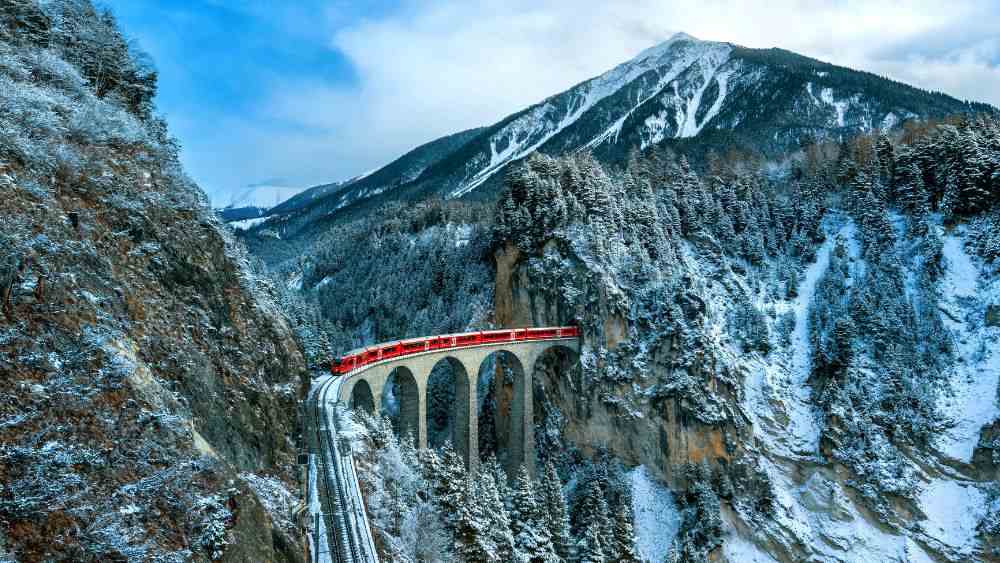 red train passing in between rock mountain