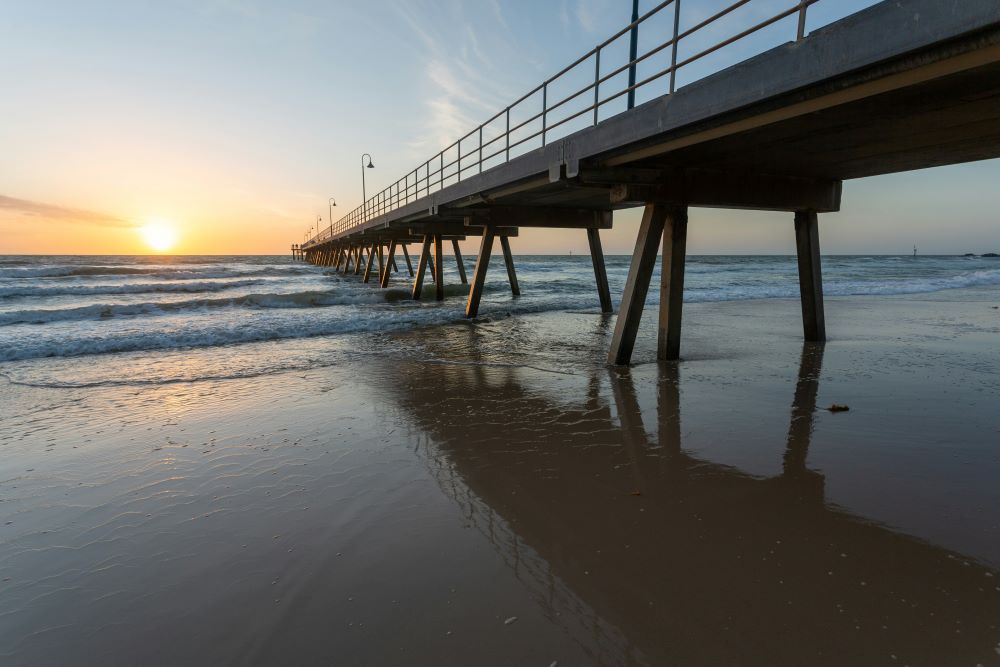 sun is setting over the ocean with jetty