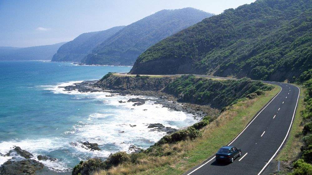 car driving at the road beside a ocean and mountain