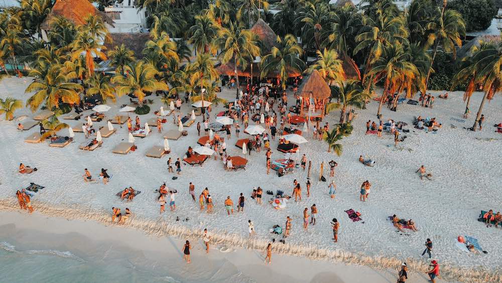 aerial view of a crowded beach all standing and sitting on a white sand