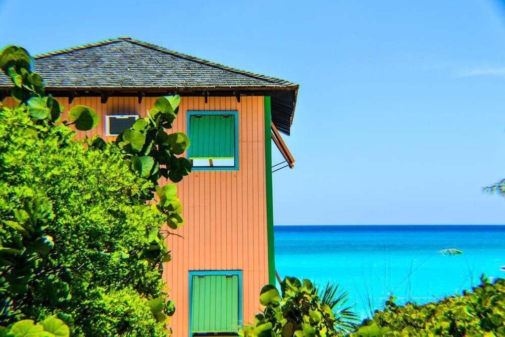 wooden house surrounded by green trees/plants and blue sea at Half Moon Beach Bahamas