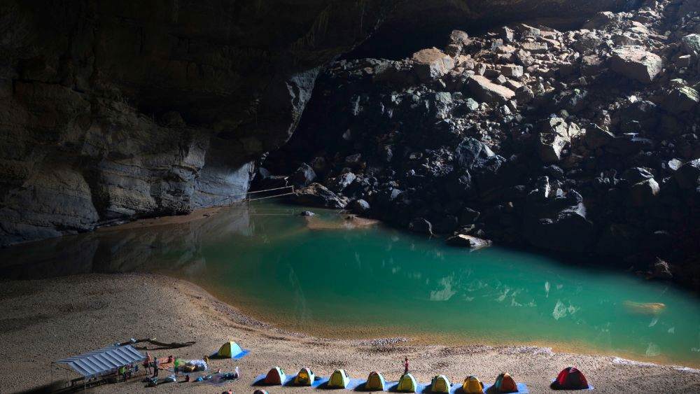 tent at the side of body of water inside the cave
