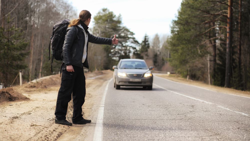 man in the road trying to stop a car signing for Hitchhiking