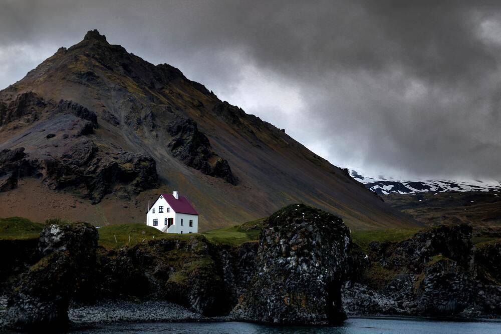 Iceland landscape showing black rock formation and mountain and 1 white house in the middle