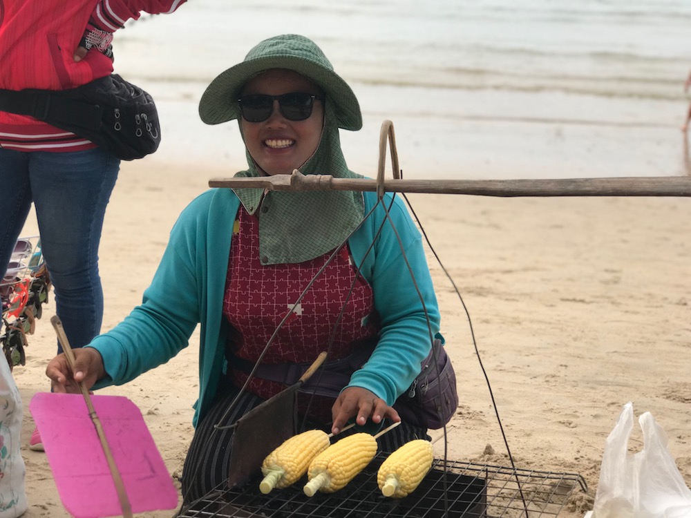 a lady smiling while selling corn in the seashore