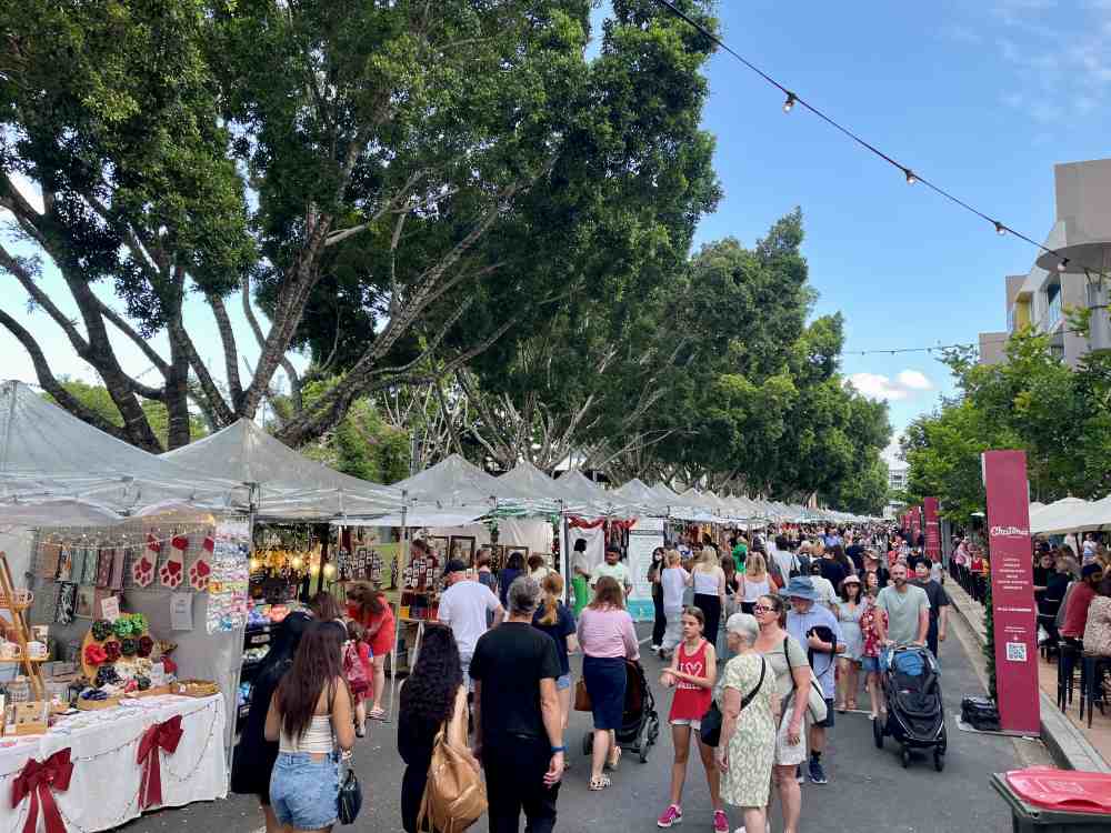 people walking in the street with stall selling on the side and cafe on the other siode