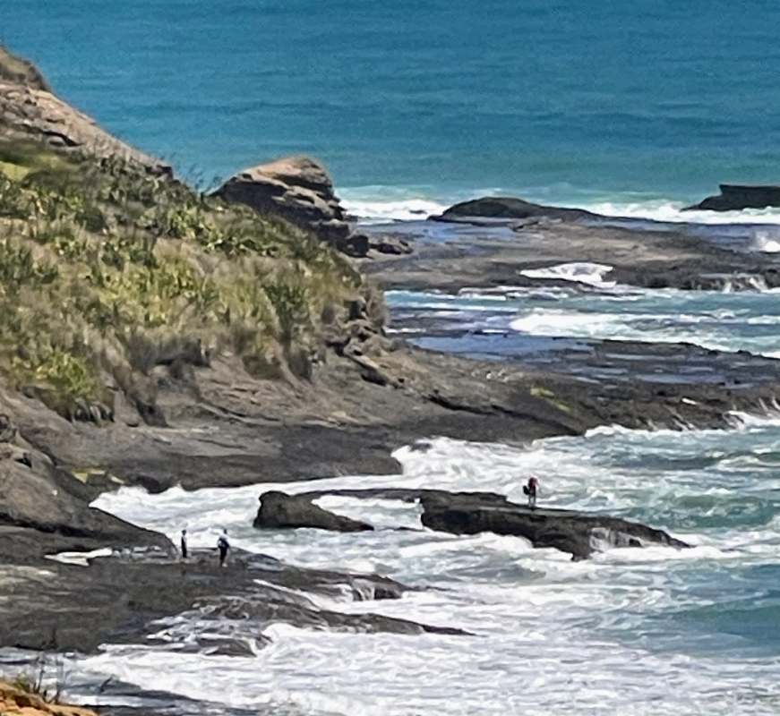 guy in the middle of the ocean on top of large rock