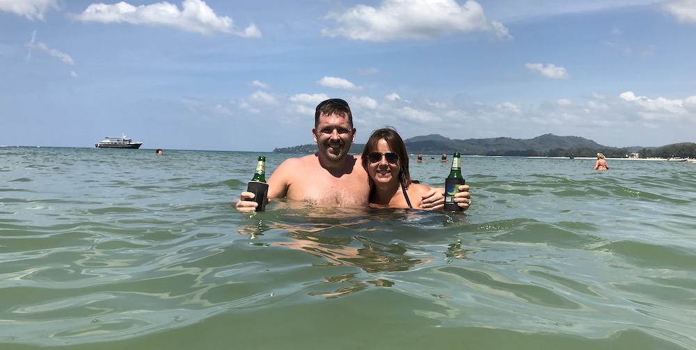 husband and I holding a beer in the beach