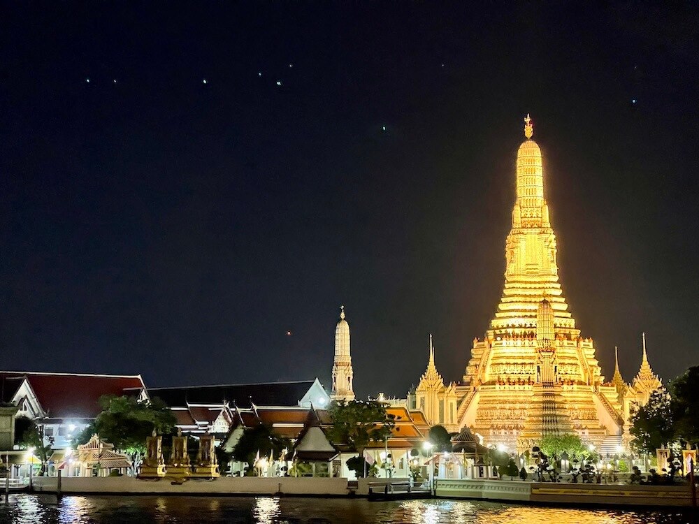 tall tower full of light with other small building near a body of water
