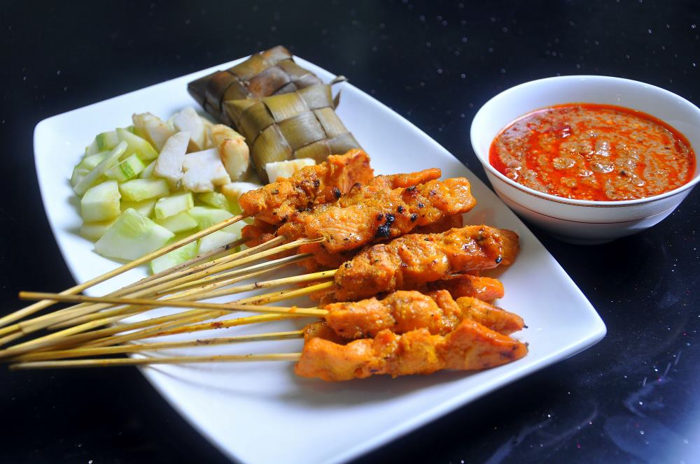 chicken skewer in a white plate beside a vegies and peanut sauce- best thai food in thailand