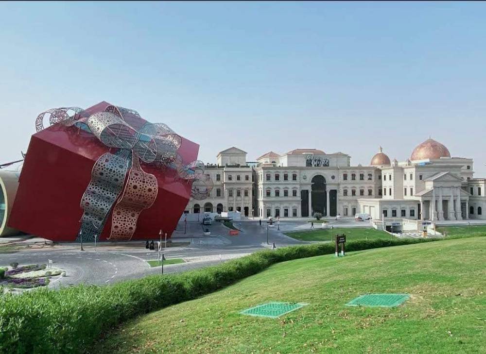 The red “Gift Box” Sculpture near building - One Day in Doha
