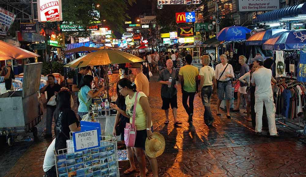 bunch of people walking around the street with clothes and foods for sale during night time