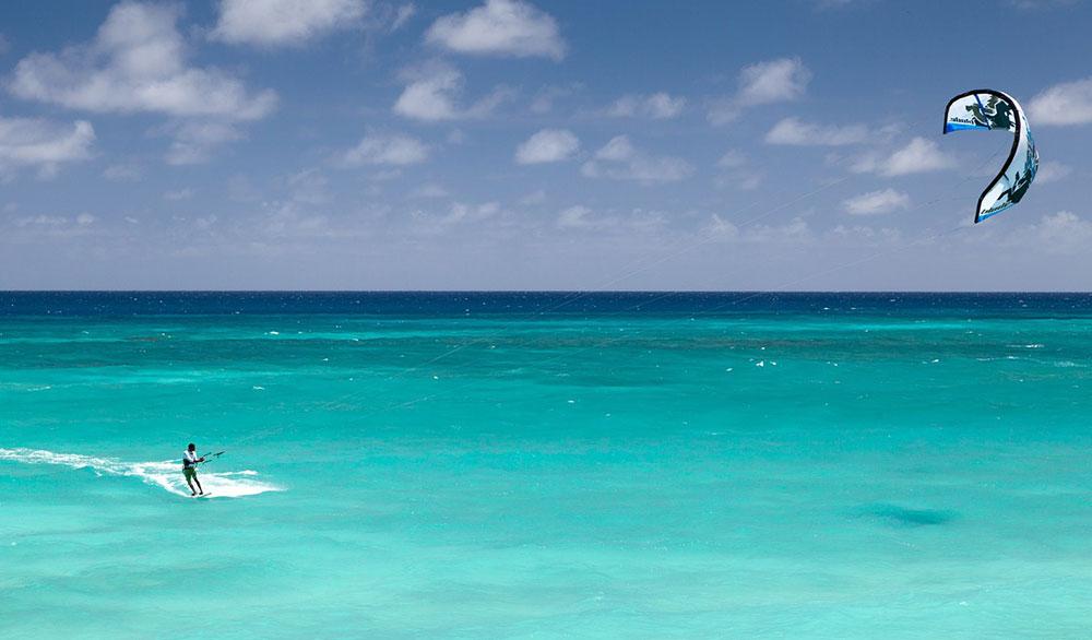 A man in surfboard kitesurfing in the green sea