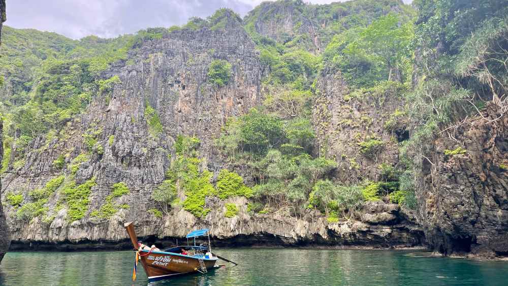 boat in the middle of the ocean with rock formation in the back - phuket vs krabi