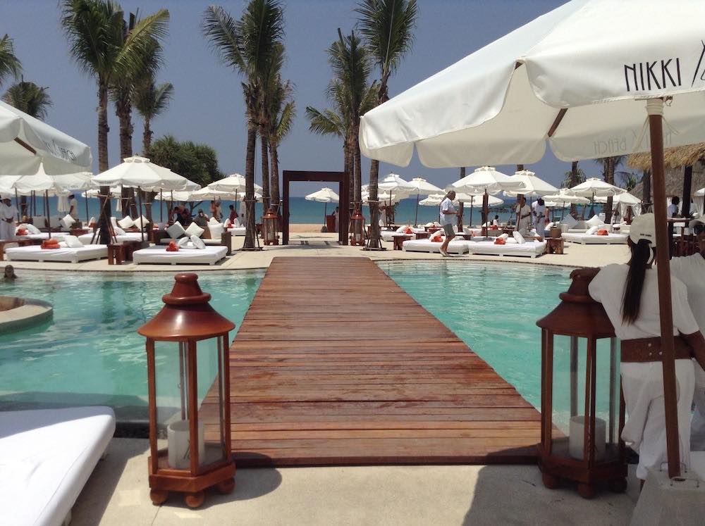 white umbrella beach beds surrounded the pool with bunch of people at the beach club