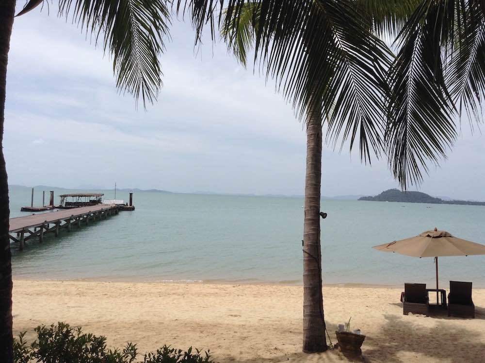 front view of a beach with coconut tree, umbrella and beach bed with wooden pathway going to the beach also known as the coconut island