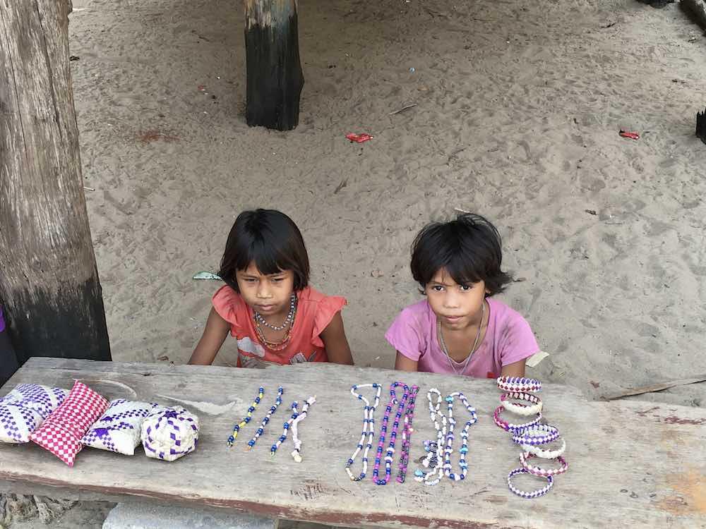 two girls sitting on the sand selling bracelets
